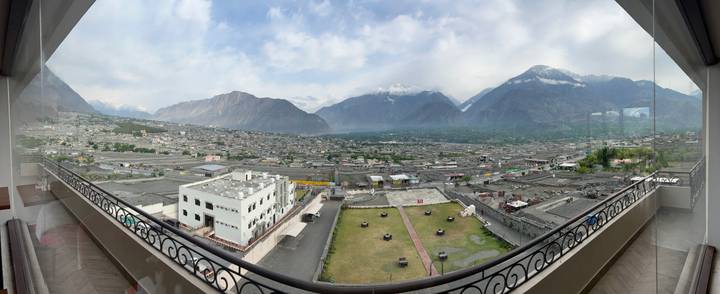 Wide panoramic cityscape framed by balcony railings with mountains rising behind the valley town.