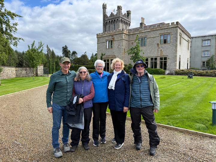 Small group standing on gravel drive in front of an Irish manor house with manicured lawn.