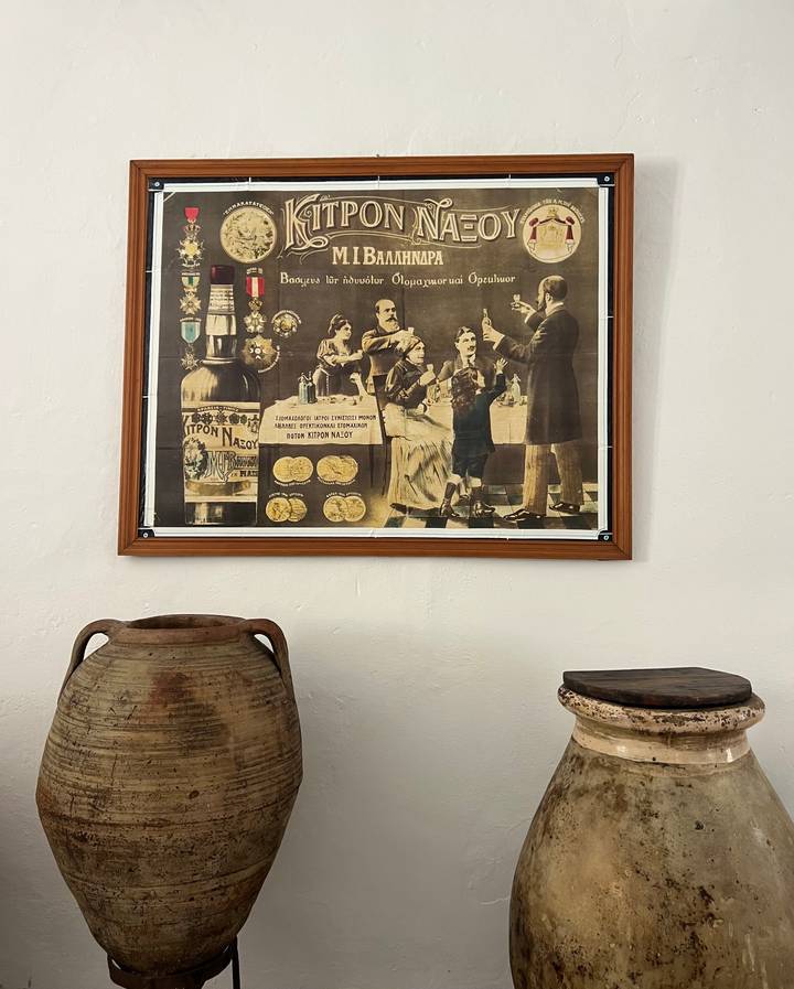 Vintage advertisement poster displayed above rustic pottery jars in a small museum corner.
