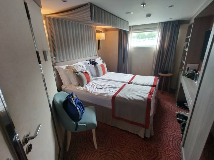 Compact river-cruise cabin with twin beds neatly made, soft lighting and a small window.