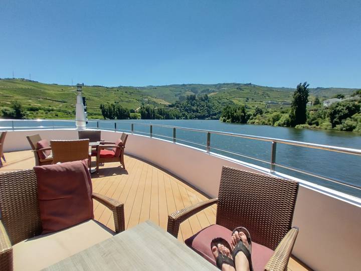 Sun-drenched open deck of a river cruise ship overlooking vine-covered Douro hills and calm water.