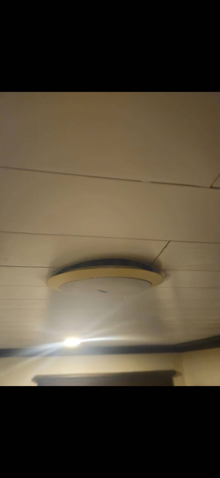 Close-up of a ceiling speaker fixture against beige paneling.