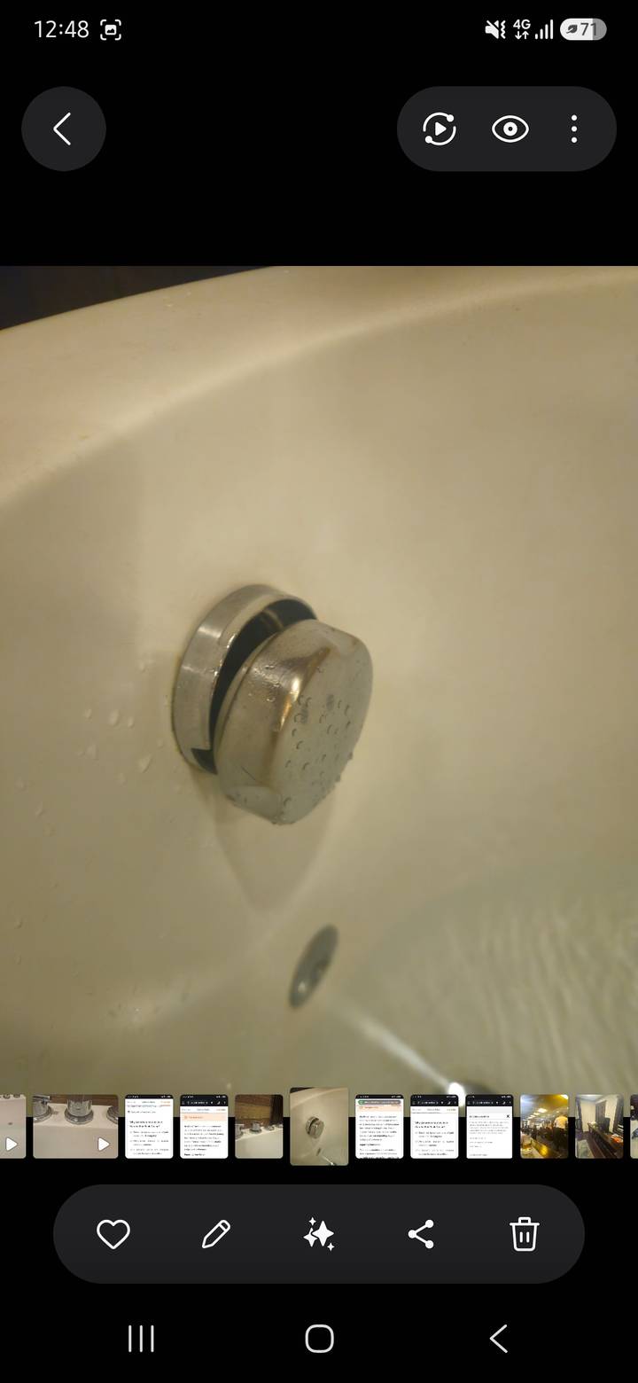 Blurry close-up of a metal bathtub plug against a pale background with water droplets.