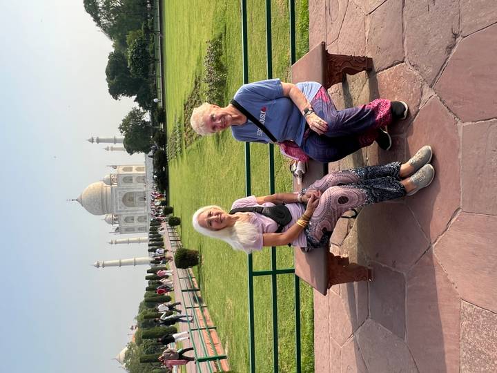 Two mature women seated on a bench with the Taj Mahal rising majestically behind them