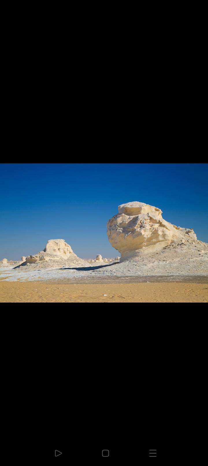 Striking white limestone rock formations rise from the desert floor under a deep blue sky.