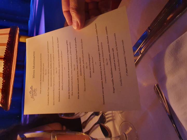 A hand holds a printed French dinner menu at a softly lit restaurant table.