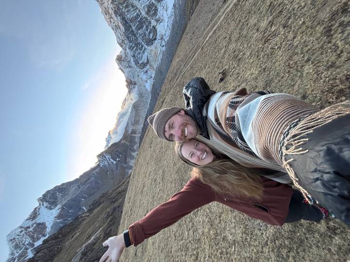 Couple in alpine meadow raising arms with snow-capped Andes peaks behind