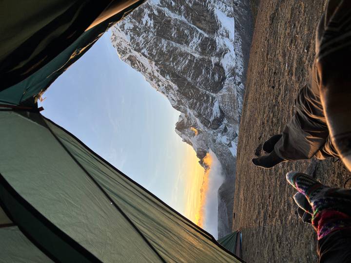 View from inside a tent framing snowy Andean peaks at dawn with travellers’ feet in view