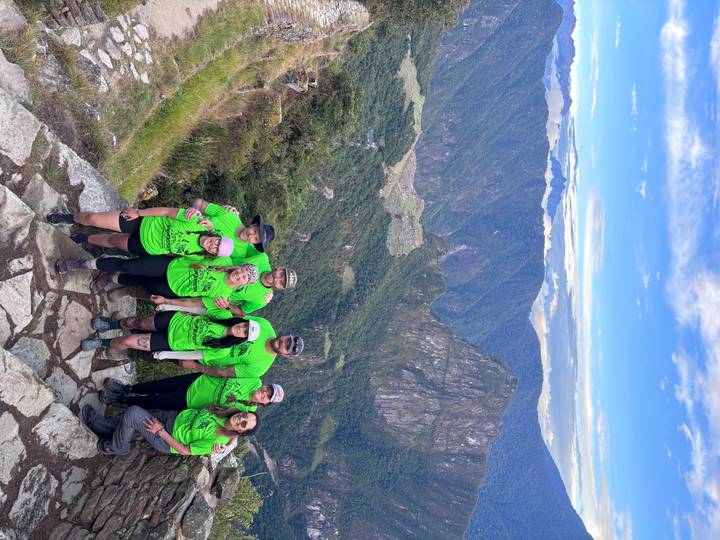 Group of trekkers in bright shirts posing on high viewpoint above Machu Picchu valley