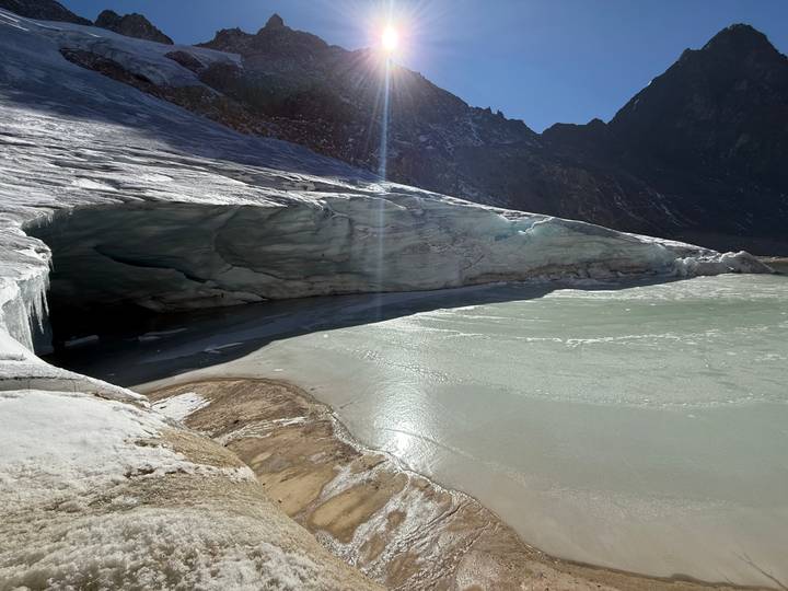 Icy glacial cave and partially frozen lake under bright alpine sun