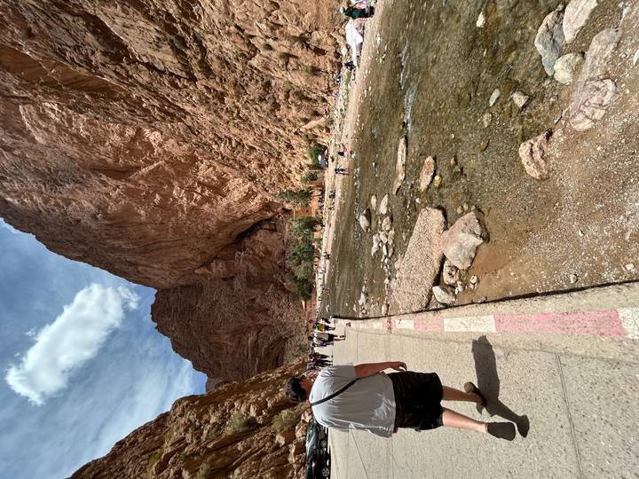 Tourists walking along river path framed by towering red cliffs of Todra Gorge