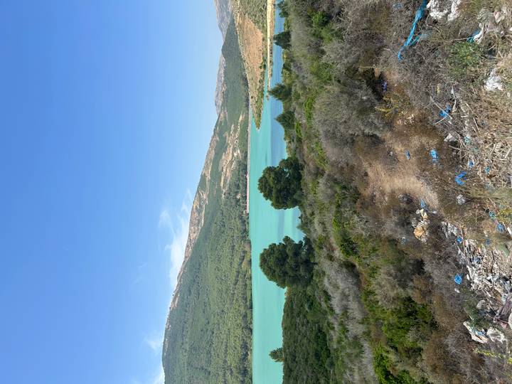 Turquoise reservoir surrounded by rolling green hills with some litter in foreground