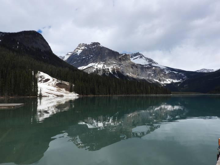 Snow-capped Rocky Mountains reflecting in a calm turquoise lake fringed by conifer forest.
