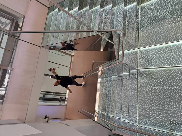 Playful portrait of a traveller stretching arms wide while standing on a futuristic glass staircase inside a modern building.