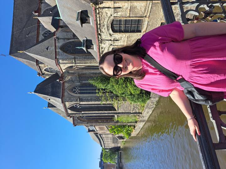 Traveller in pink dress smiling on a bridge beside the medieval church towers and canal of Ghent on a bright sunny day.