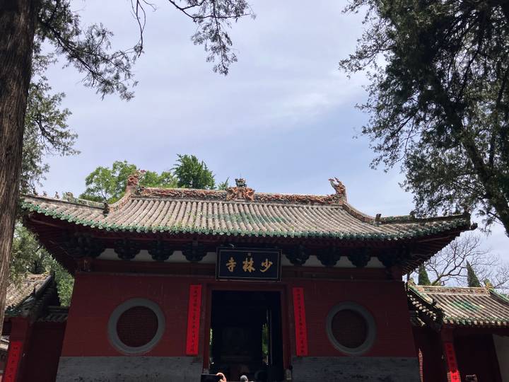 Entrance gate of Shaolin Temple adorned with ornate roof carvings and a black sign under clear skies.