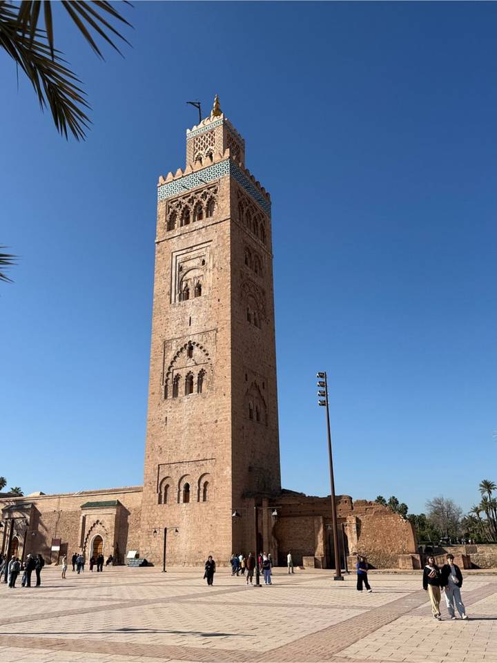 The tall sandstone Koutoubia Mosque minaret rises against a clear blue sky.
