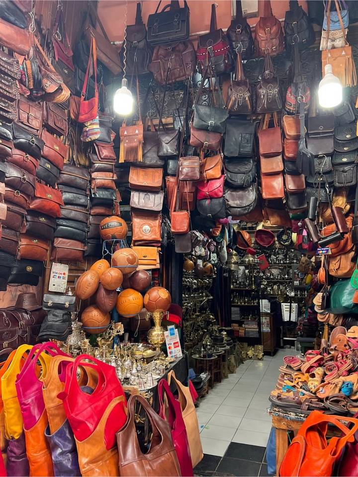 Tightly packed stall displaying leather bags, vintage footballs and brassware in the Marrakesh souk.