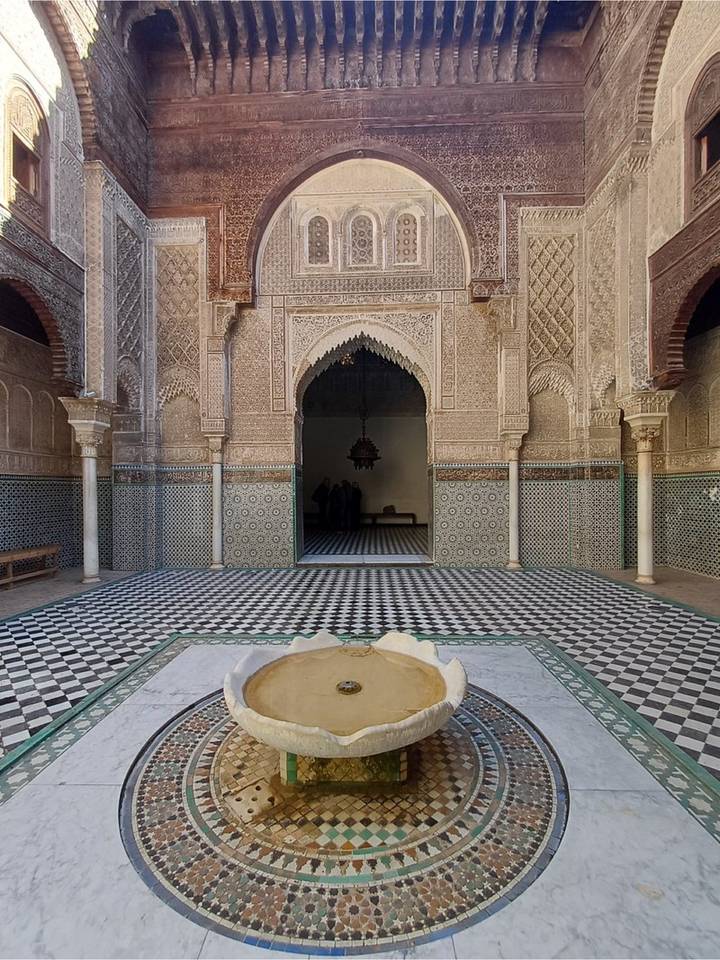 Quiet tiled courtyard with central fountain and intricately carved archway inside a Moroccan palace.