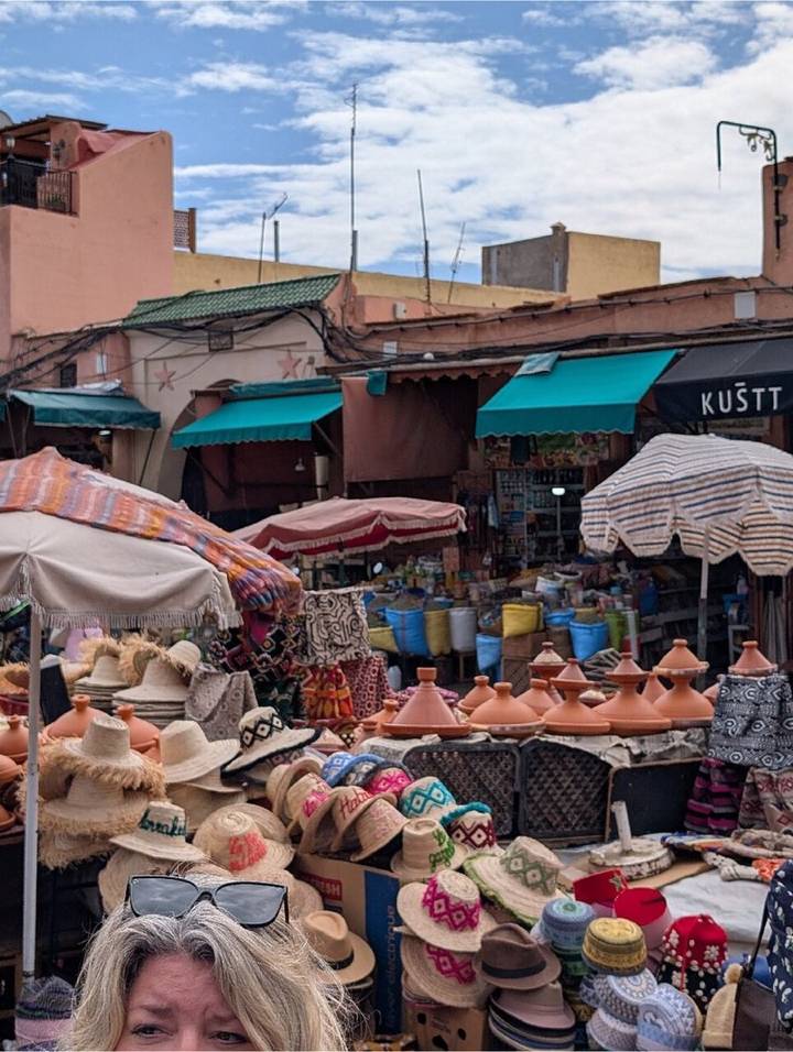 Market square scene with tagine pots, striped parasols and sacks of goods under colourful awnings.