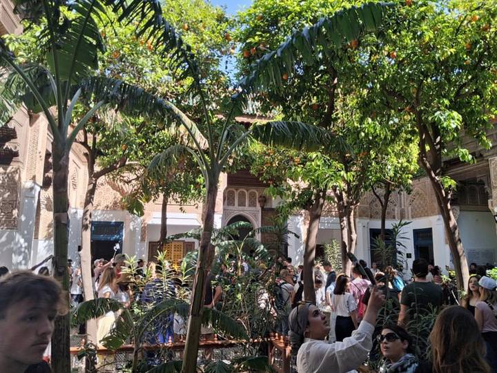 Busy courtyard garden in Marrakesh filled with tourists under orange trees and palms