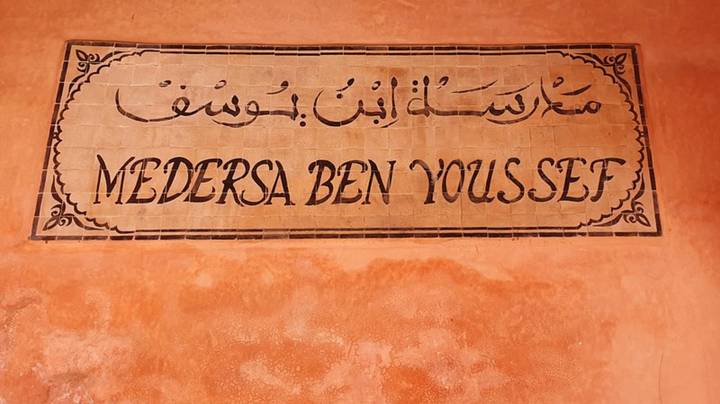 Tile sign reading 'Medersa Ben Youssef' mounted on an ochre wall