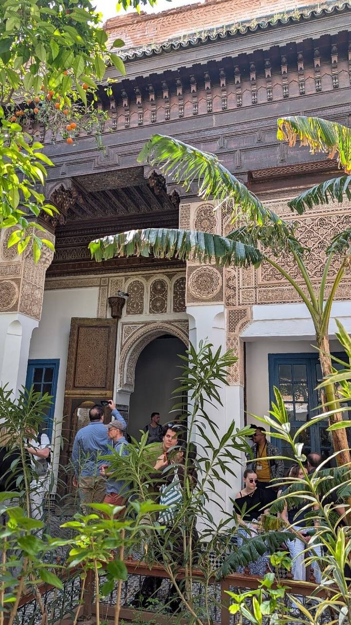 Courtyard corner with carved arches, palm leaves and a visitor taking photos