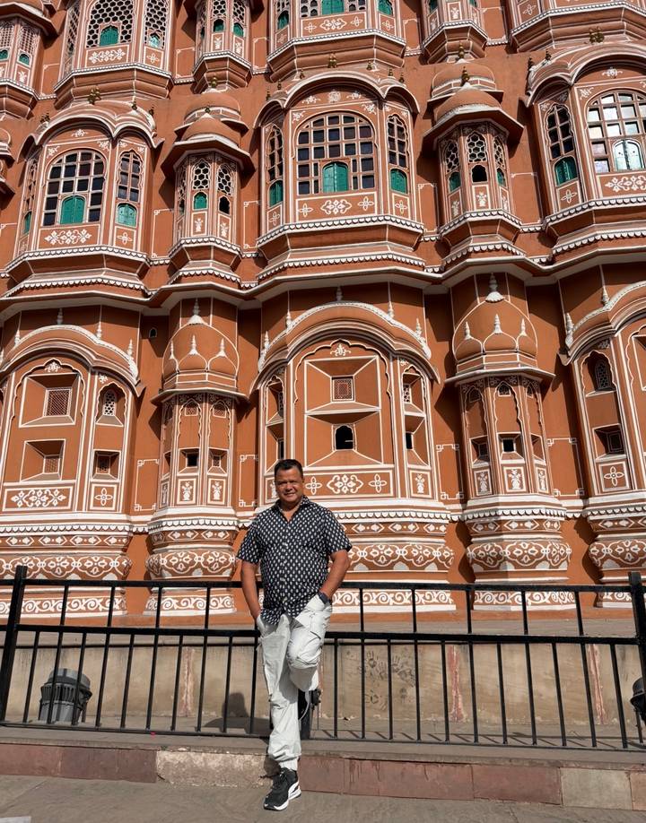 Visitor stands before intricate terracotta façade decorated with white motifs in Jaipur.