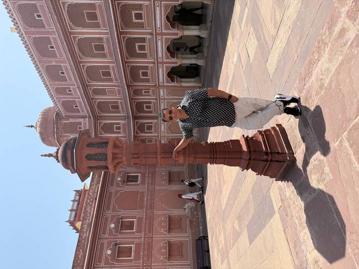 Visitor leans against a red sandstone lamp post in the spacious courtyard of Jaipur City Palace.