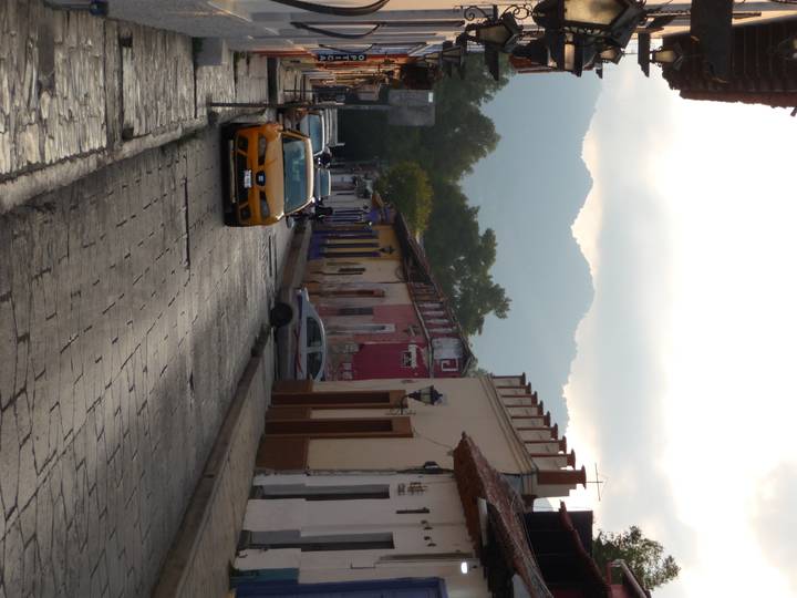 A cobbled colonial street lined with colorful low-rise houses, mountains rising in the hazy background.