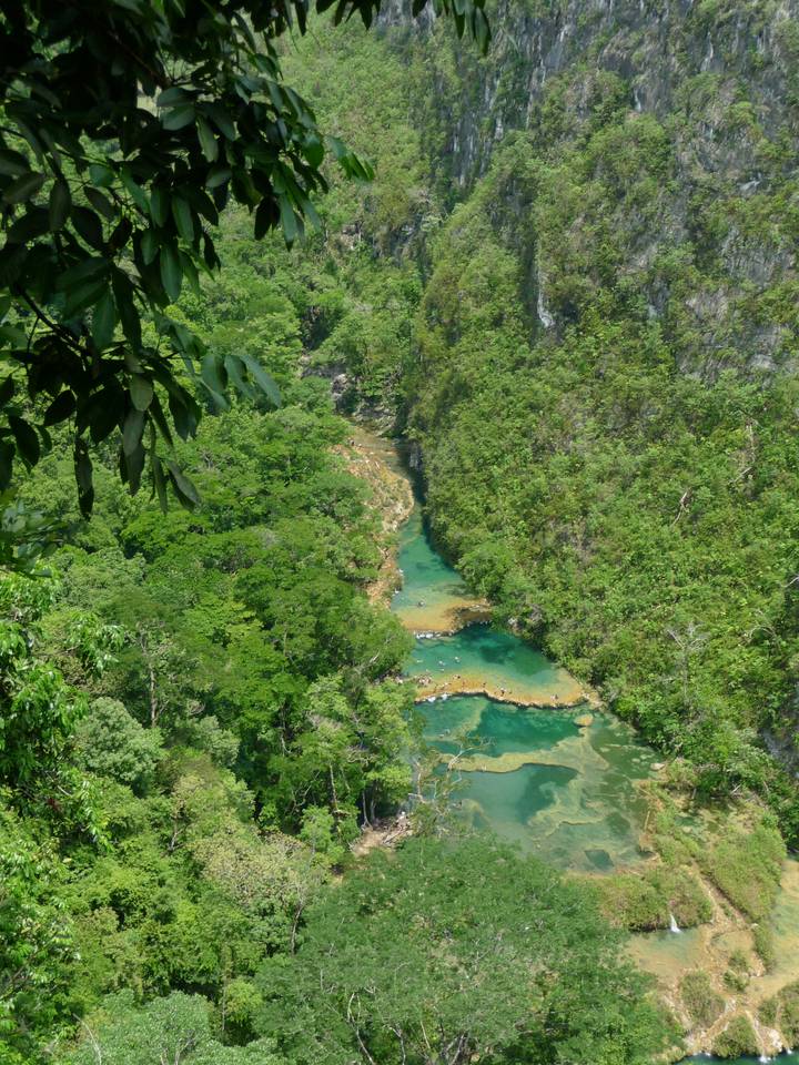An emerald river with turquoise limestone pools winding through dense tropical jungle seen from above.