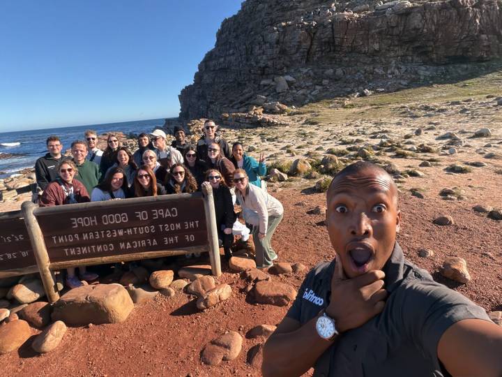 Duplicate angle of tour group selfie at Cape of Good Hope with dramatic rocky coast behind.