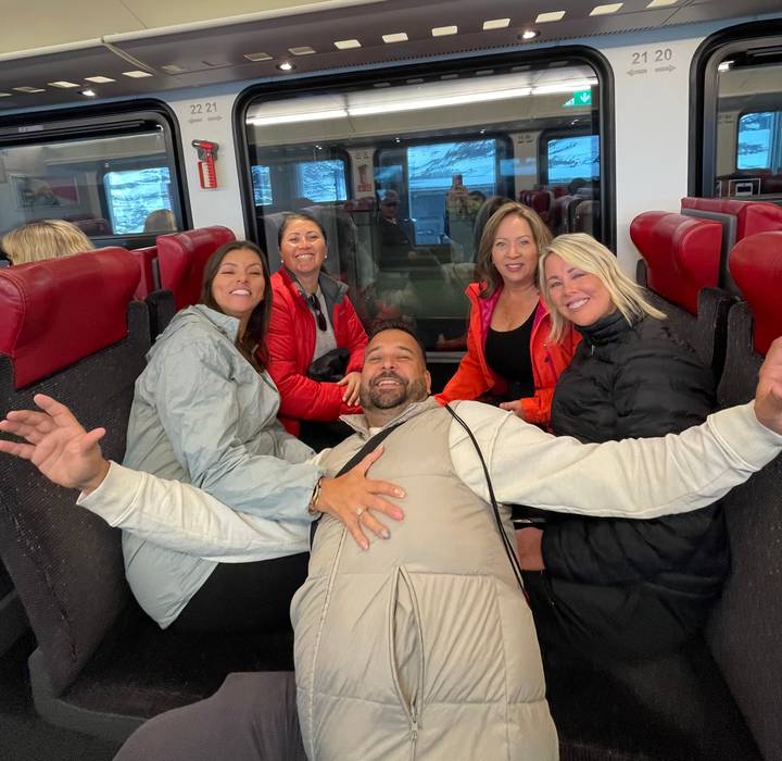 Travellers laugh together while seated on red train seats during an alpine rail journey.