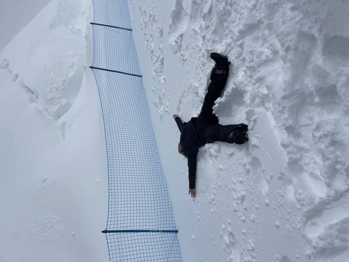 Person lies spread-eagled making a snow angel on a high-altitude snowy slope.