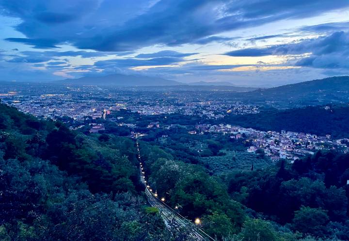 Elevated panoramic view over an Italian city valley with evening lights under dramatic clouds and blue sunset tones