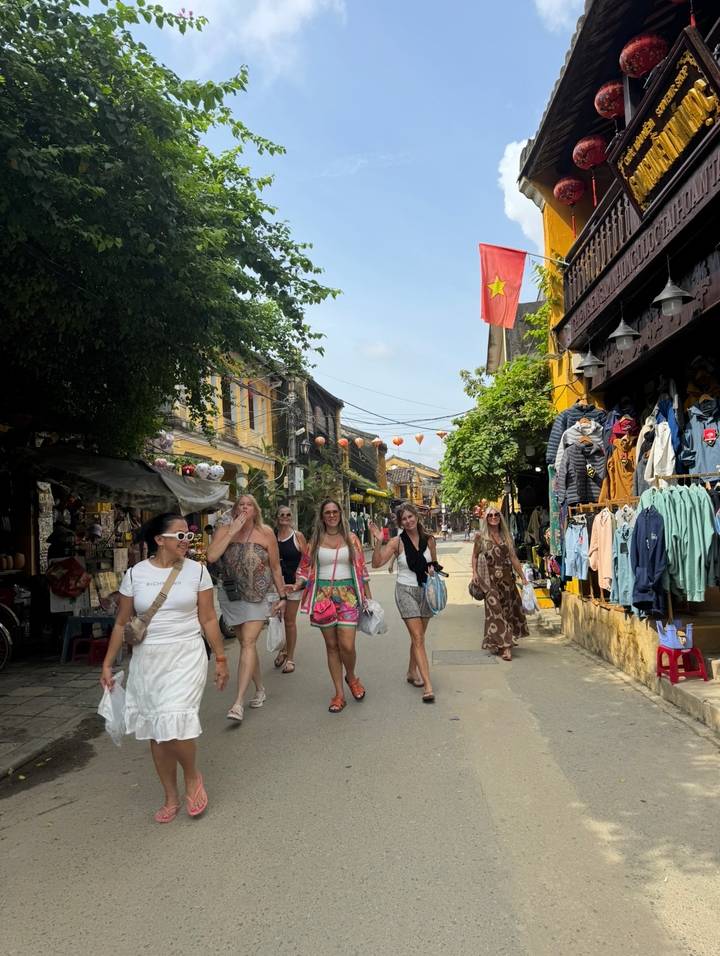 Group of women strolling through a lantern-lined market street with colorful shops and Vietnamese flag overhead