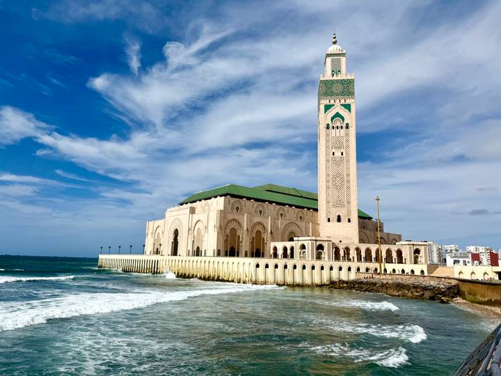 The Hassan II Mosque rises over crashing Atlantic waves beneath blue skies.