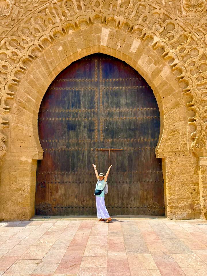 Traveller celebrating before an enormous ornate wooden gate of an ancient fort.