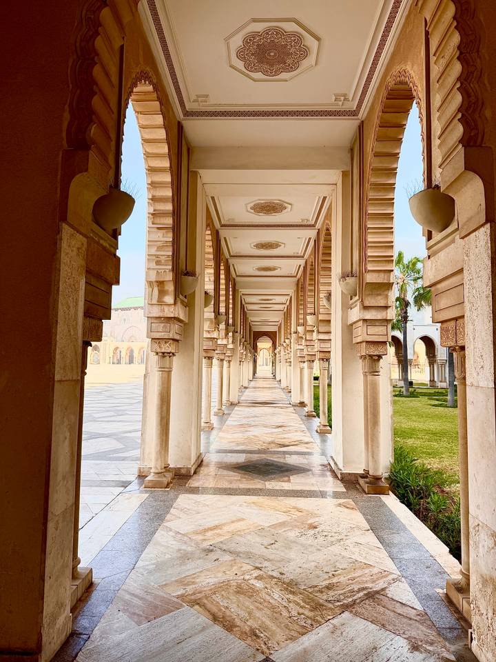 Elegant marble arcade with repeating arches and ornate ceilings in a Moroccan mosque complex.