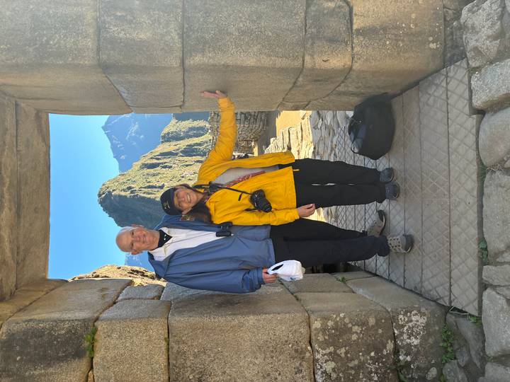 Smiling couple poses in a stone doorway overlooking the terraces and peaks of Machu Picchu.