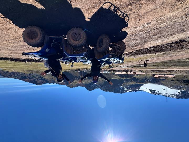 Two travellers on blue quad bikes celebrating in rugged Andean highlands with snow-capped peaks behind