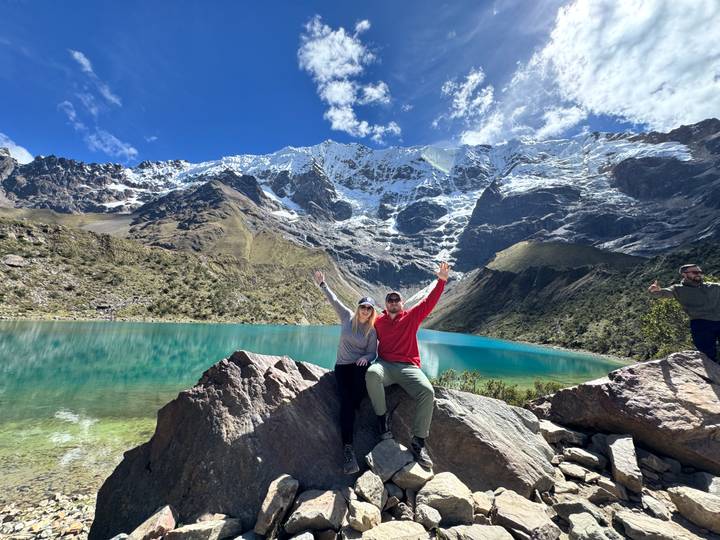 Couple posing on rock beside turquoise alpine lake with glacier-covered Andes towering behind