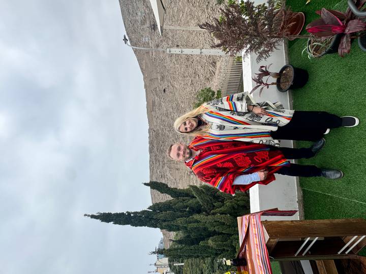 Couple dressed in colourful Andean capes posing on a rooftop garden with arid hillside behind