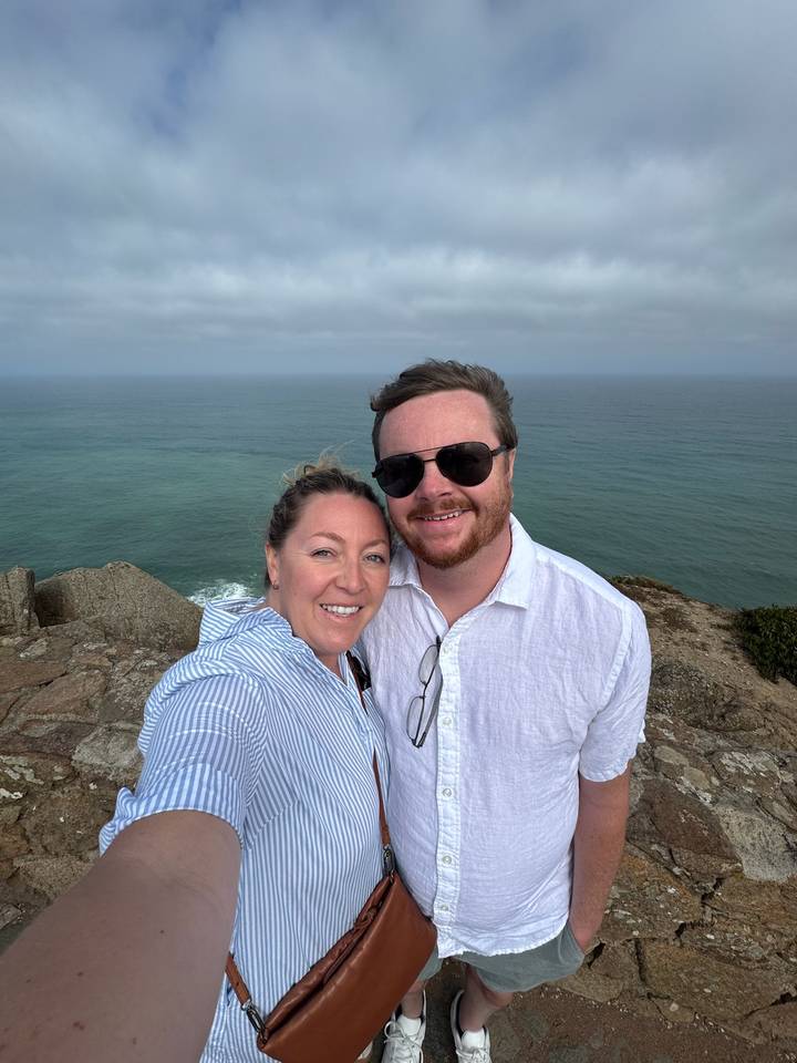 Couple selfie atop rugged Atlantic cliff with vast ocean backdrop under hazy sky