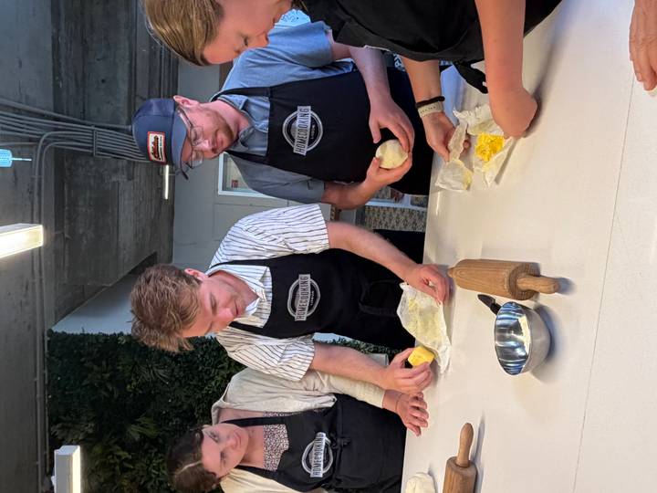 Participants in cooking class wearing aprons kneading dough around a preparation table