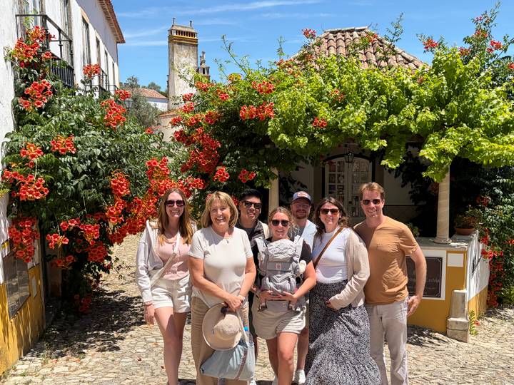 Travellers posing in a flower-filled alley of a whitewashed village under bright sunlight