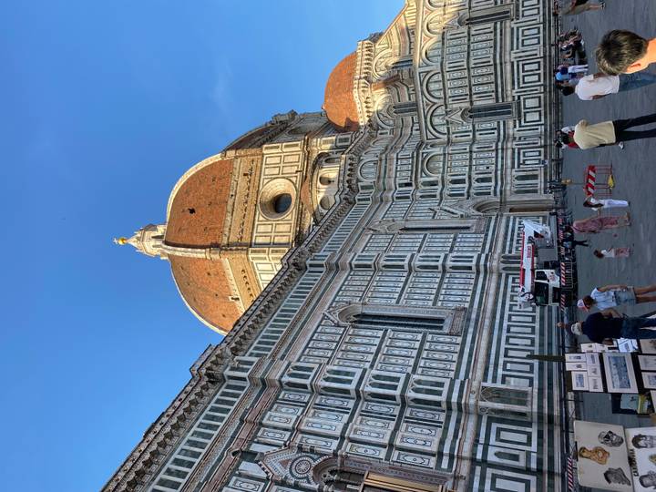 The iconic dome of Florence’s Duomo dominates the piazza bathed in warm late-day light as tourists wander below.