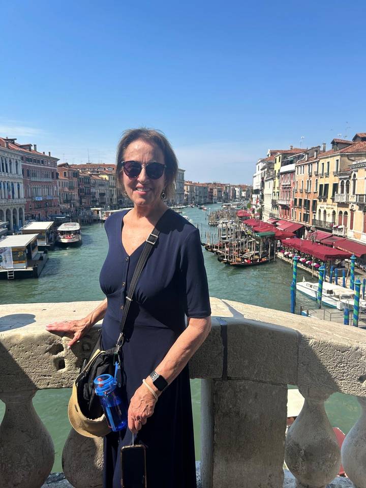 Traveller poses on a stone bridge overlooking Venice’s bustling Grand Canal lined with colourful buildings.