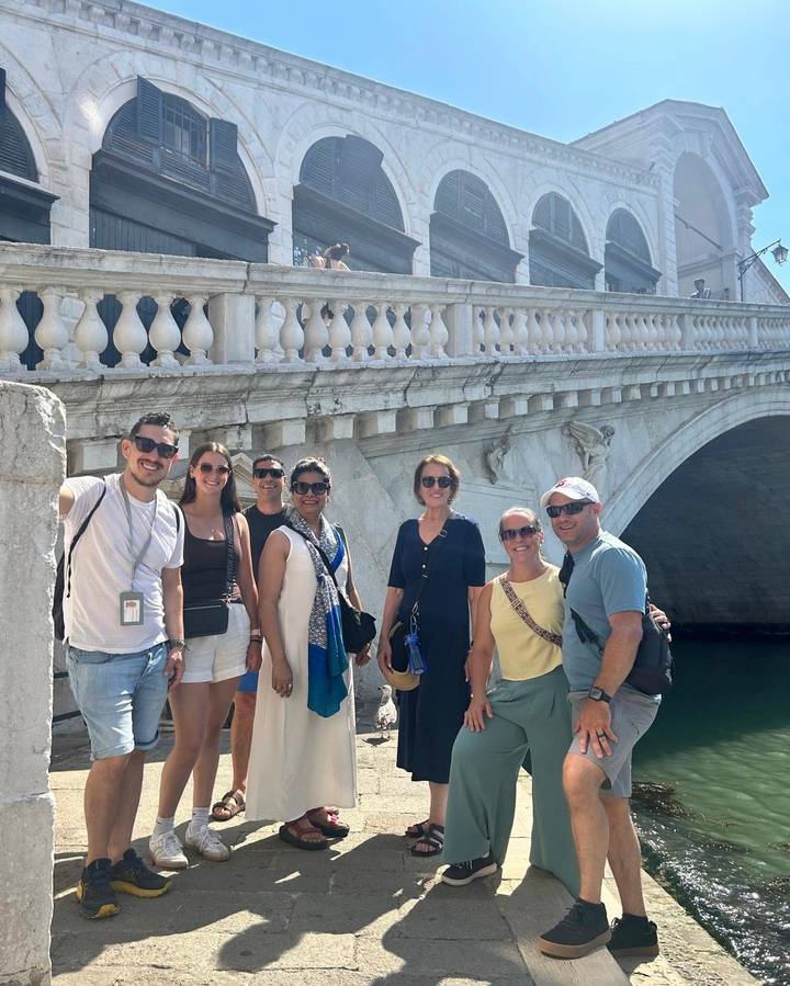 Group photo in front of Venice’s stone Rialto Bridge balustrade on a sunny day.