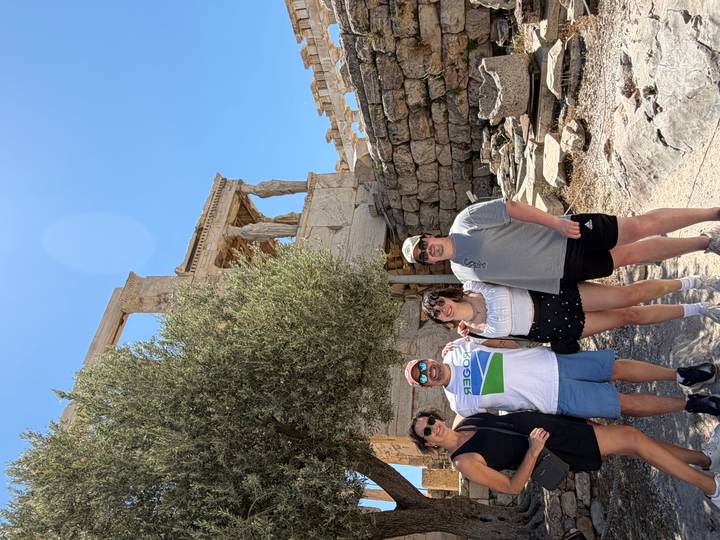 Family group poses below the Caryatid Porch of the Erechtheion on the Acropolis under bright sun.